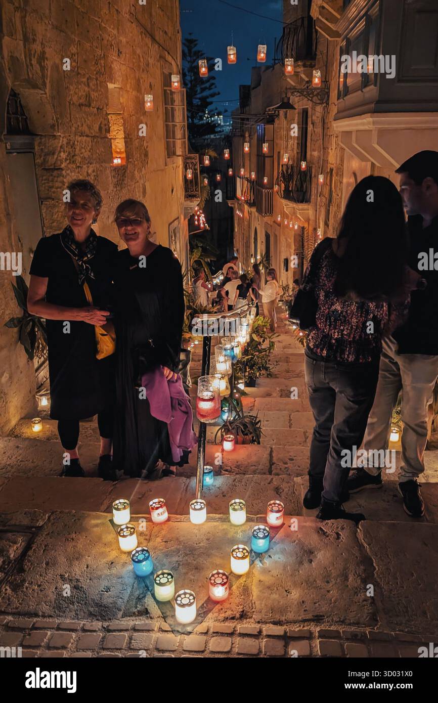 Les foules marchent dans l'allée historique maltaise bordée de bougies colorées pendant le festival Birgu à Birgu la nuit : Birgu, Malte - 11 octobre 2025 Banque D'Images