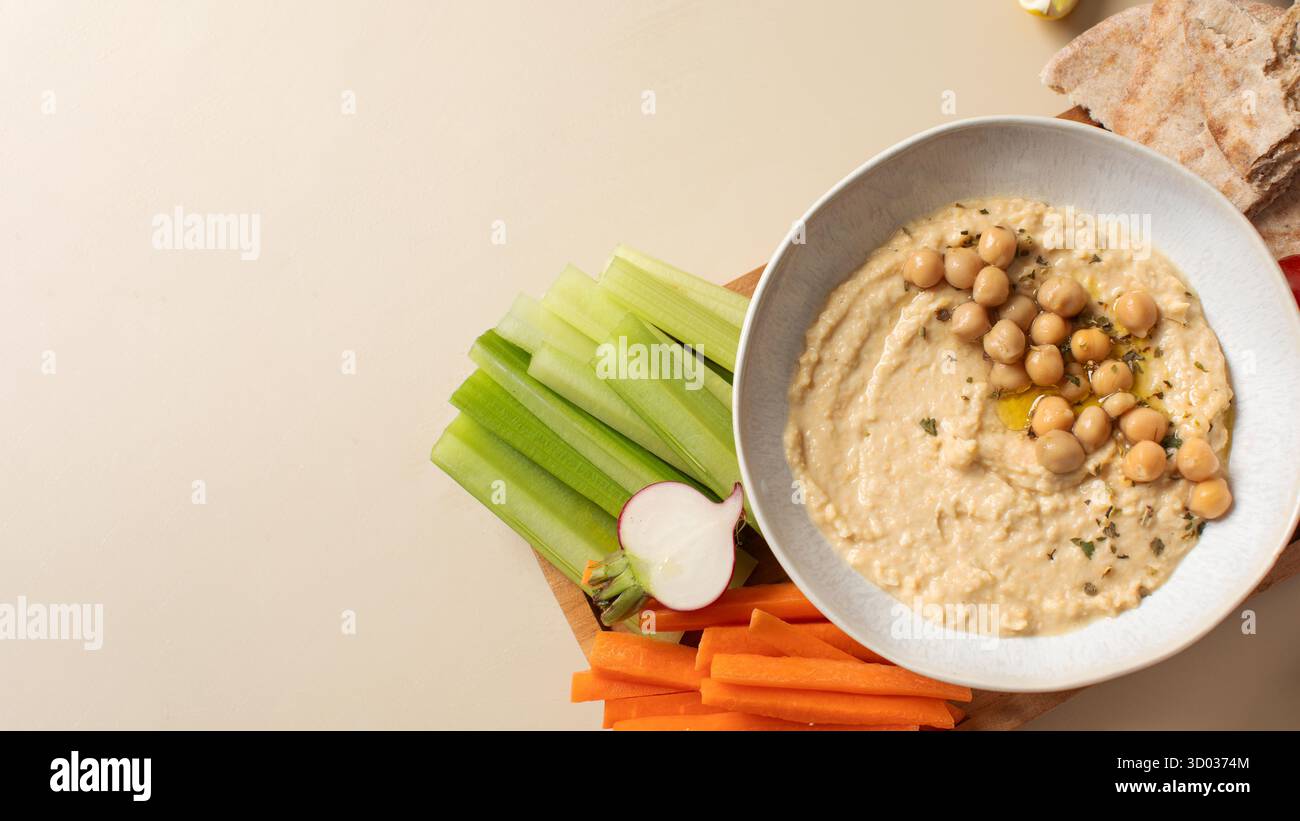 Houmous frais dans un bol sur une planche de bois avec pita, céleri et carottes. Plats de pois chiches, plat végétarien. Nourriture saine. Copier l'espace Banque D'Images