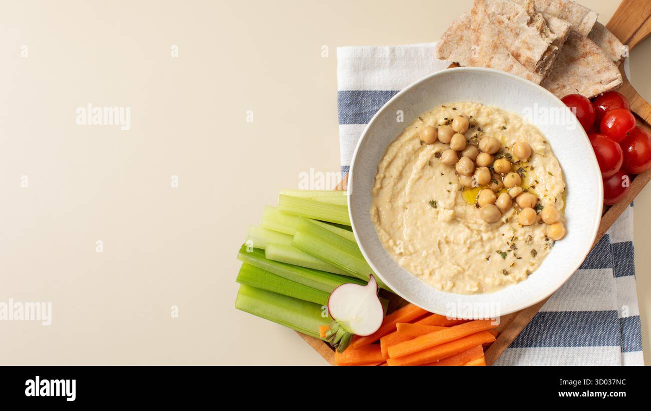 Houmous frais dans un bol sur une planche de bois avec pita, céleri et carottes. Plats de pois chiches, plat végétarien. Nourriture saine. Copier l'espace Banque D'Images