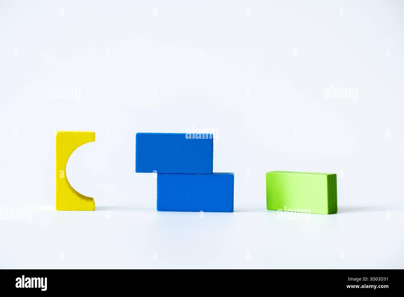 Blocs de bois jaune, vert et bleu assortis disposés dans une disposition dispersée et abstraite sur fond blanc propre, soulignant la créativité et la simplicité Banque D'Images