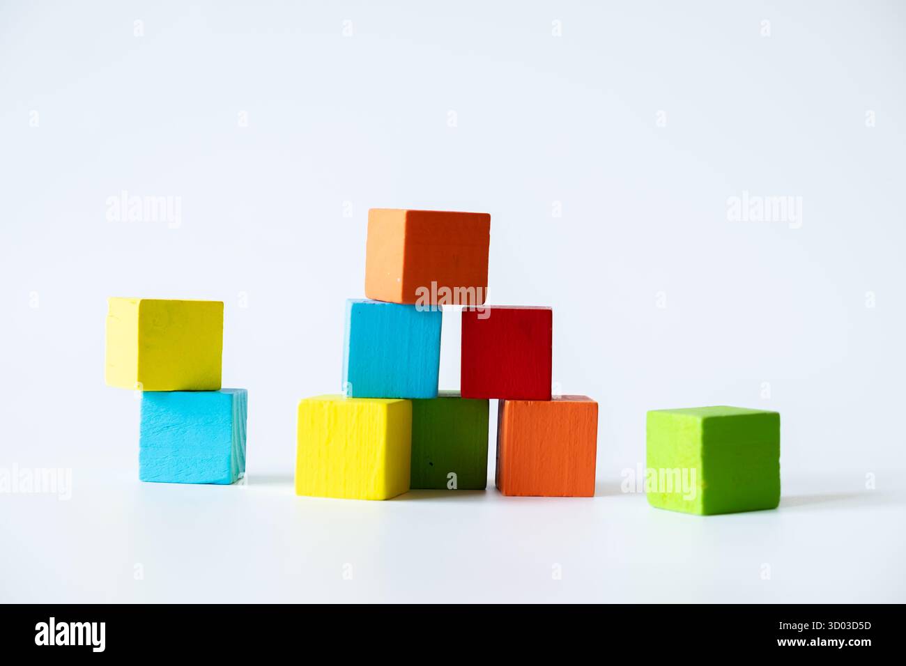 Blocs cubes en bois colorés assortis, y compris bleu, vert, jaune, rouge, et orange, arrangé de manière créative sur un fond blanc pour un apprentissage abstrait Banque D'Images