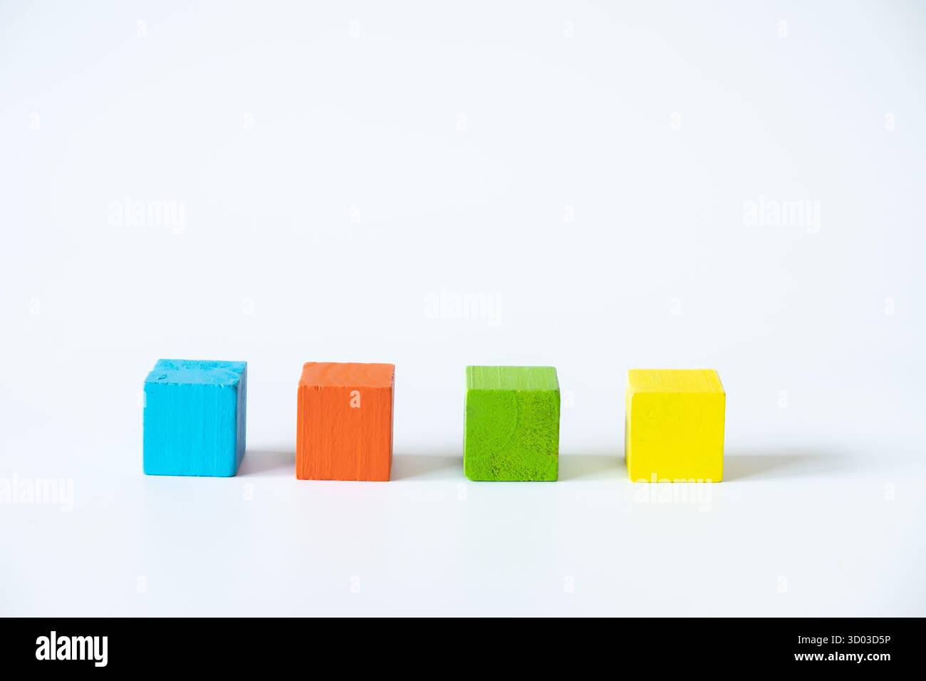 Arrangement simple de blocs cubes en bois bleu, orange, vert et jaune dans une rangée sur un fond blanc, soulignant le minimalisme, l'apprentissage et le créati Banque D'Images