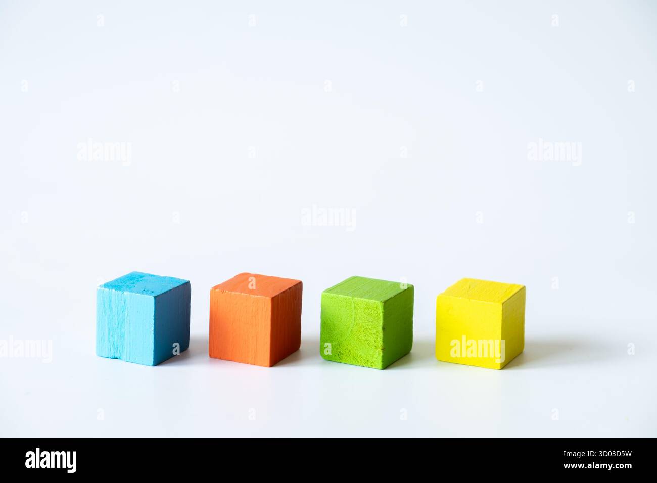 Composition minimale de cubes en bois bleu, orange, vert et jaune alignés sur un fond blanc, représentant la créativité, l'apprentissage et le si Banque D'Images