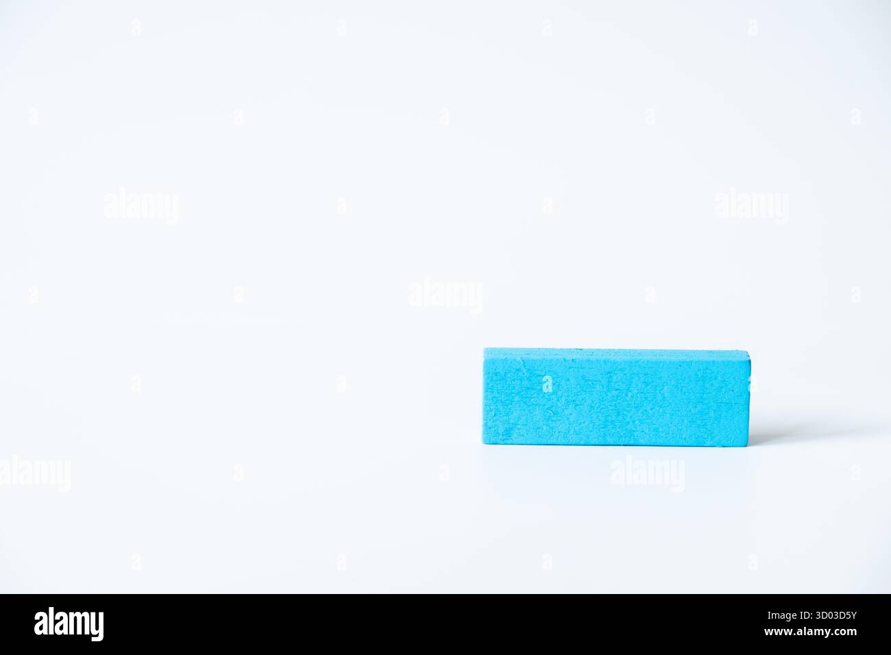 Bloc de bois bleu isolé sur fond blanc dans une composition minimaliste, représentant la simplicité, la créativité et l'apprentissage de base. Banque D'Images