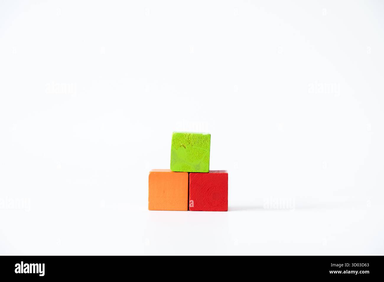Trois cubes en bois colorés en vert, orange et rouge empilés dans un arrangement pyramidal simple sur un fond blanc propre, symbolisant la créativité et Banque D'Images