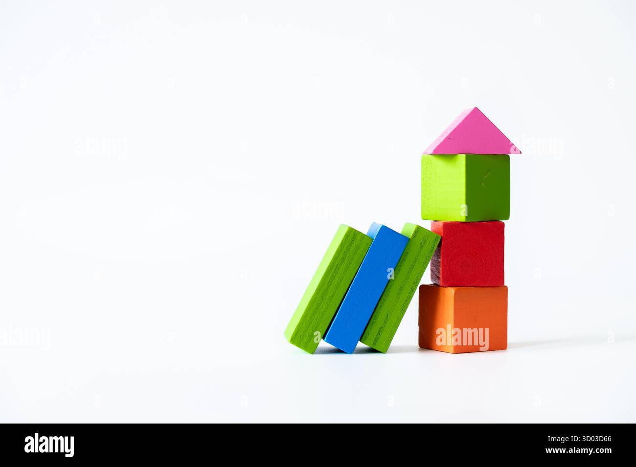 Blocs de jouets en bois colorés empilés verticalement pour ressembler à une maison, avec des blocs verts et bleus supplémentaires penchés latéralement, le tout isolé sur un bac blanc Banque D'Images