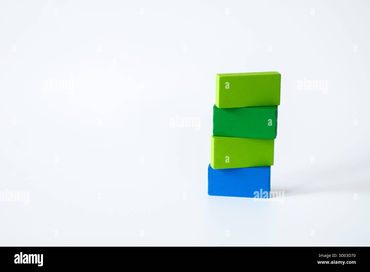 Trois blocs de bois rectangulaires verts et un bleu empilés dans un arrangement créatif sur un fond blanc, représentant l'apprentissage, la croissance et le simplisme Banque D'Images