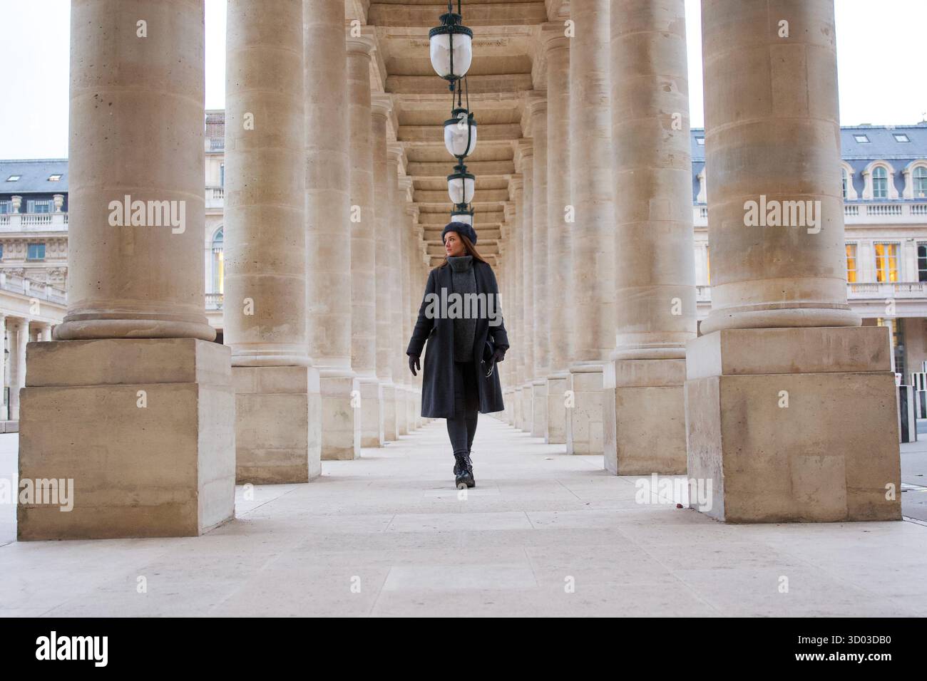 Une femme à la mode en vêtements d'hiver marche entre les colonnes de pierre du Palais Royal. Le design symétrique et le style parisien créent une scène intemporelle et élégante. Photo de haute qualité || autorisation du modèle Banque D'Images