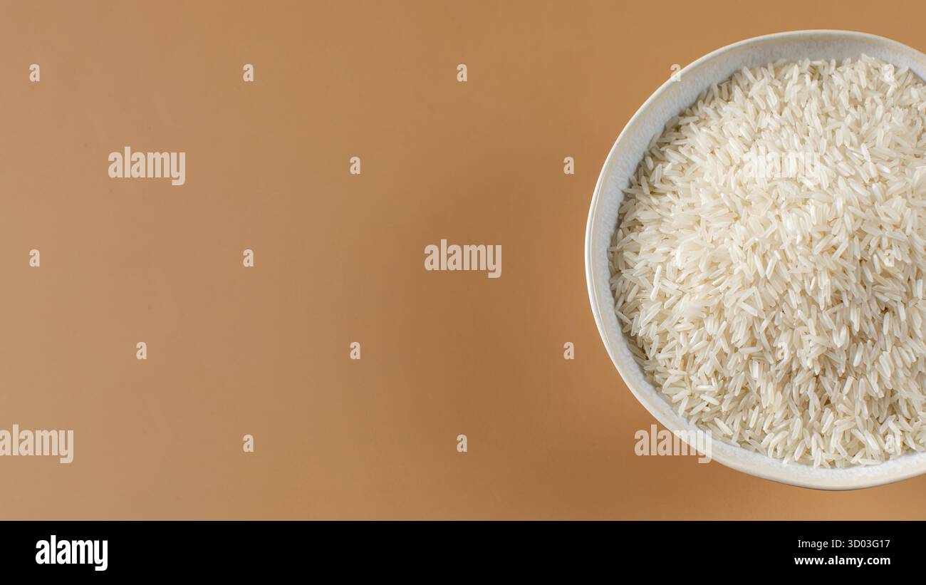 Bol de riz basmati aromatique sur fond marron clair vue supérieure. Grains longs non cuits pour une cuisson saine des plats. Modèle de maquette pour la publicité Banque D'Images