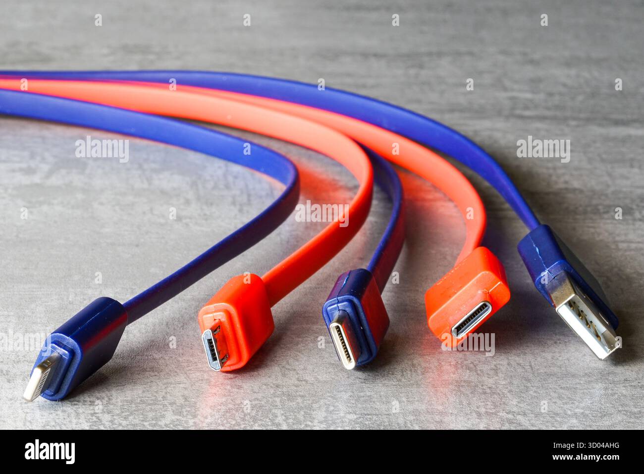 Gros plan des câbles de chargement USB, Micro USB et USB-C rouges et bleus sur une surface grise, symbolisant la technologie, le transfert de données et la connectivité Banque D'Images
