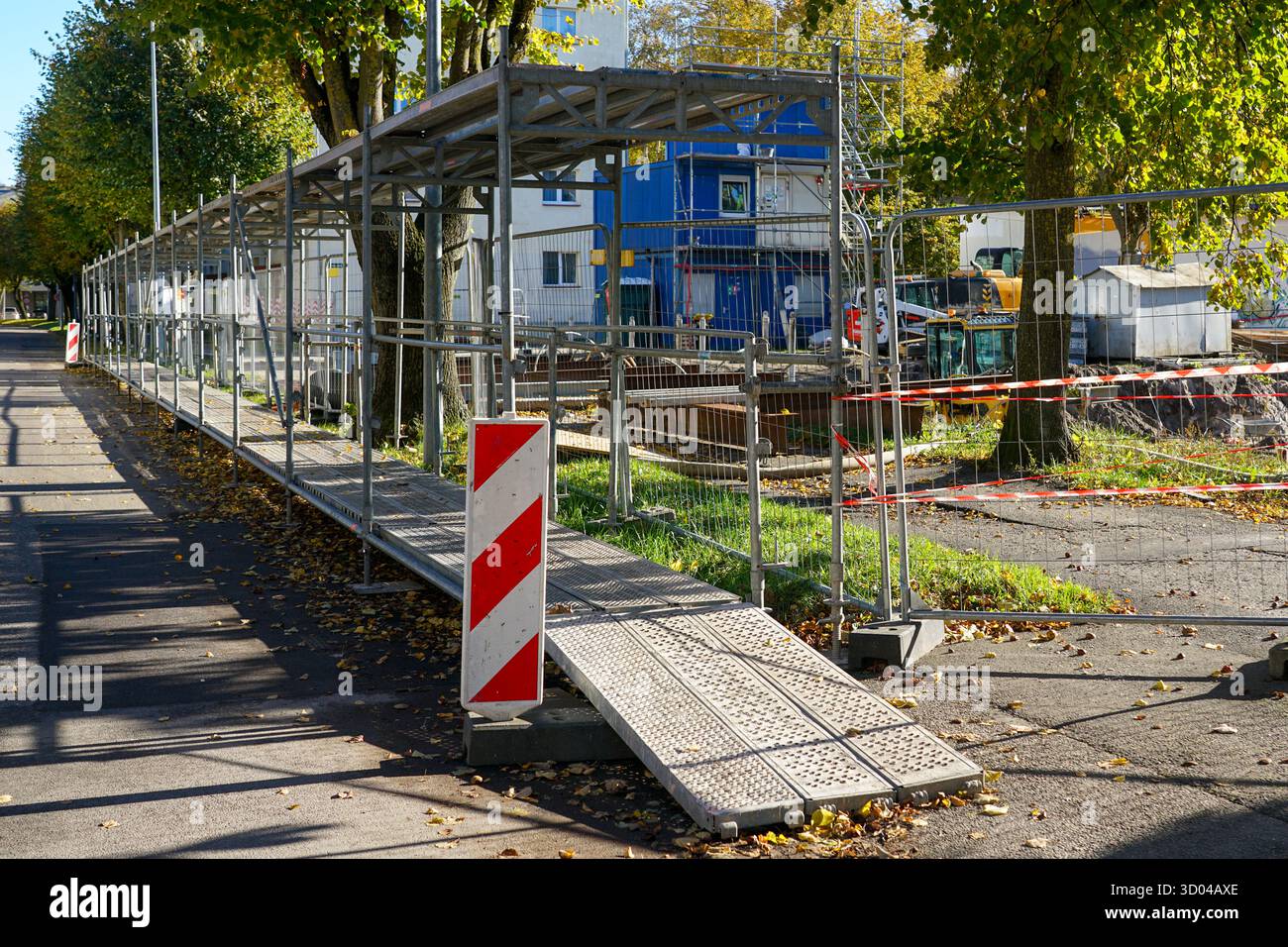 Passage piétonnier temporaire sécurisé avec échafaudages métalliques et barrières de sécurité le long d'un chantier de construction actif dans une zone urbaine pendant l'automne Banque D'Images