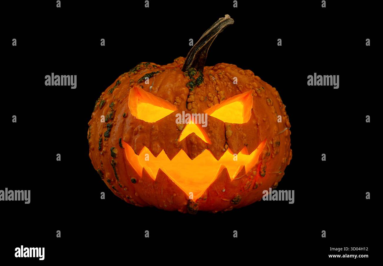 Traditionnel Jack-o'-lanterne effrayant visage souriant brillant dans le noir, isolé sur un fond noir, fabriqué à partir d'une citrouille pour célébrer Halloween. Banque D'Images