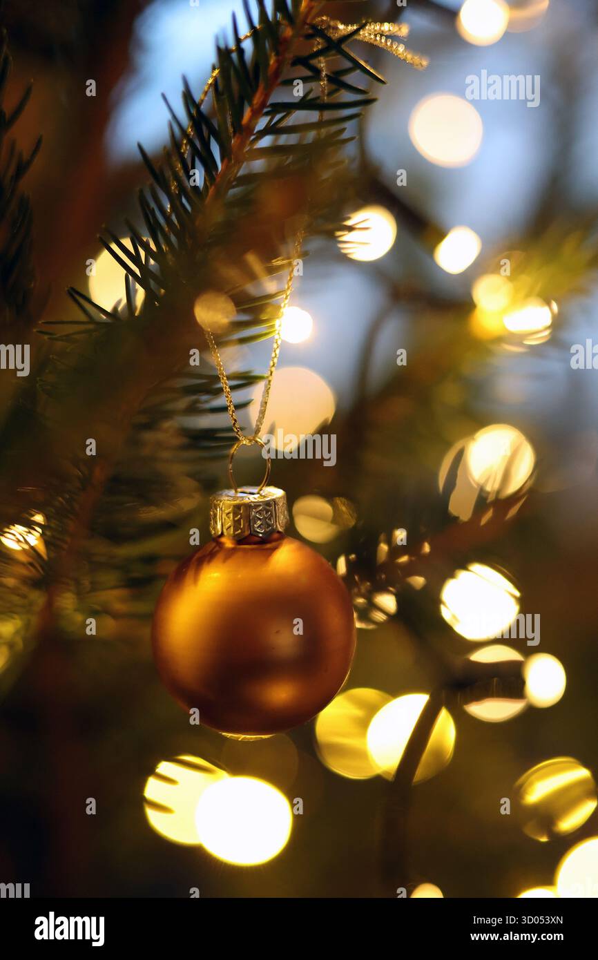 Boule dorée mate suspendue à une branche d'arbre de Noël par des lumières bokeh chaudes en arrière-plan Banque D'Images