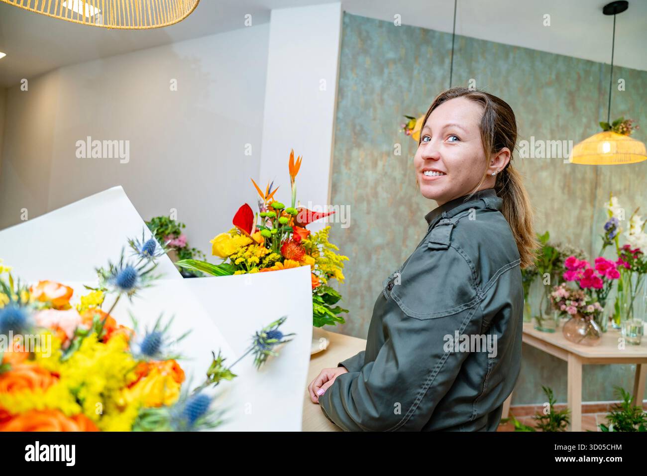 Femme souriante, présentant des arrangements floraux dans un magasin de fleurs contemporain Banque D'Images
