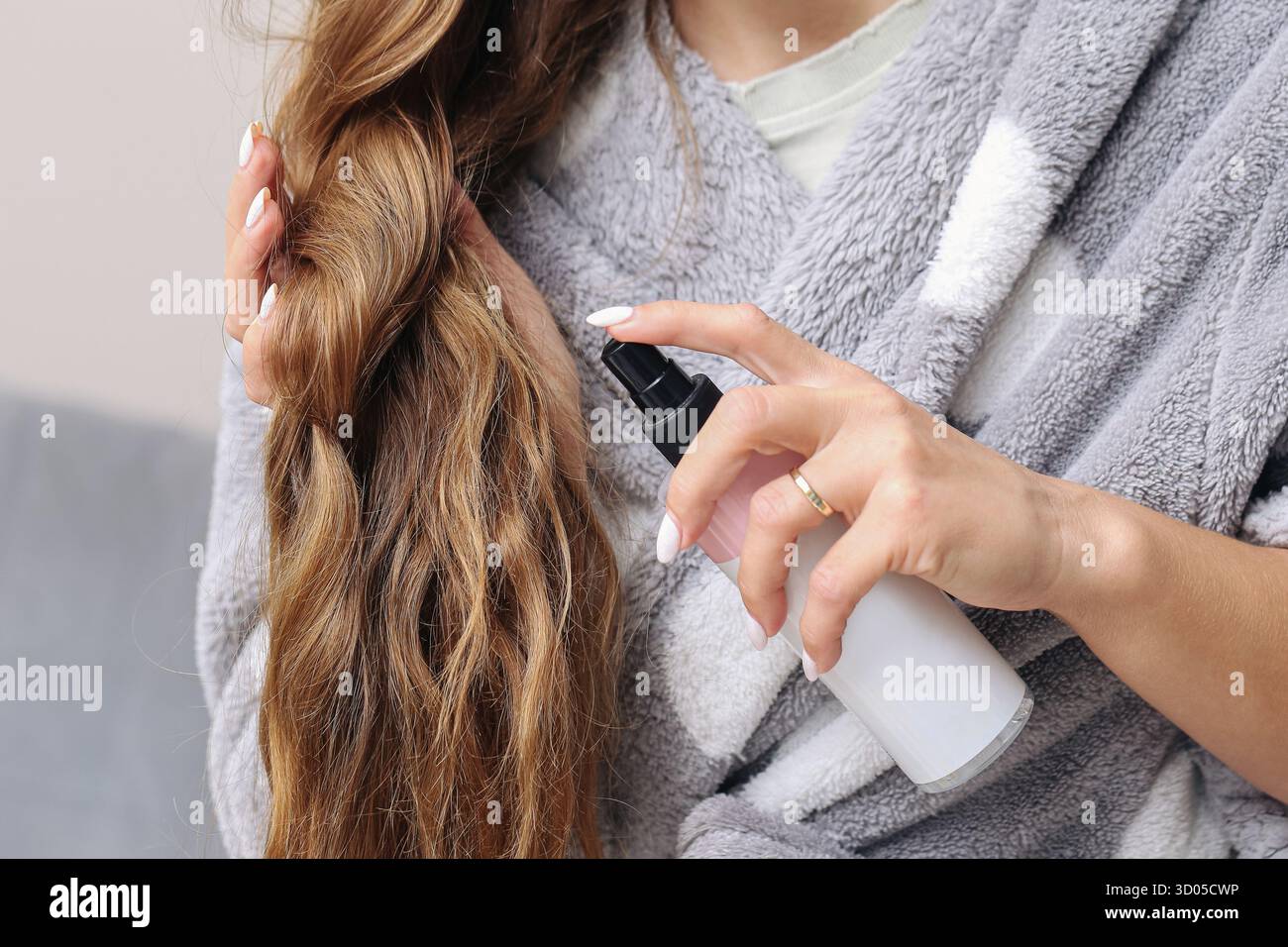 Femme pulvérisant les cheveux avec la brume cosmétique. Soins capillaires et routine beauté à la maison. Concept de cheveux brillants sains et autosoins. Banque D'Images