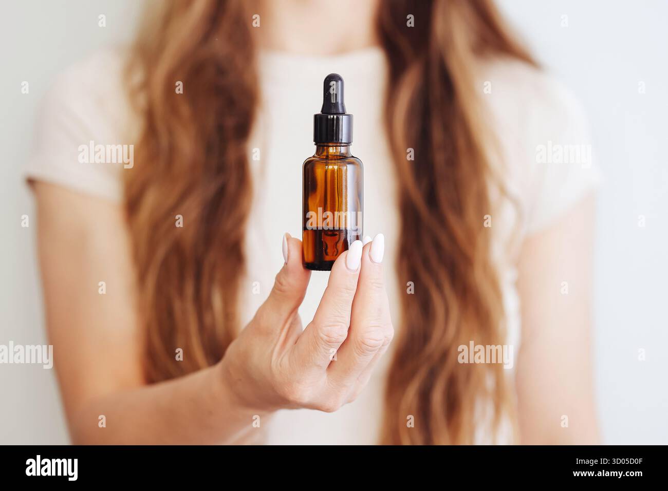 Femme tenant un flacon compte-gouttes ambré. Présentoir de sérum de soin de la peau. Cosmétiques naturels en main. Concept de routine beauté. Fond de studio minimal. Banque D'Images