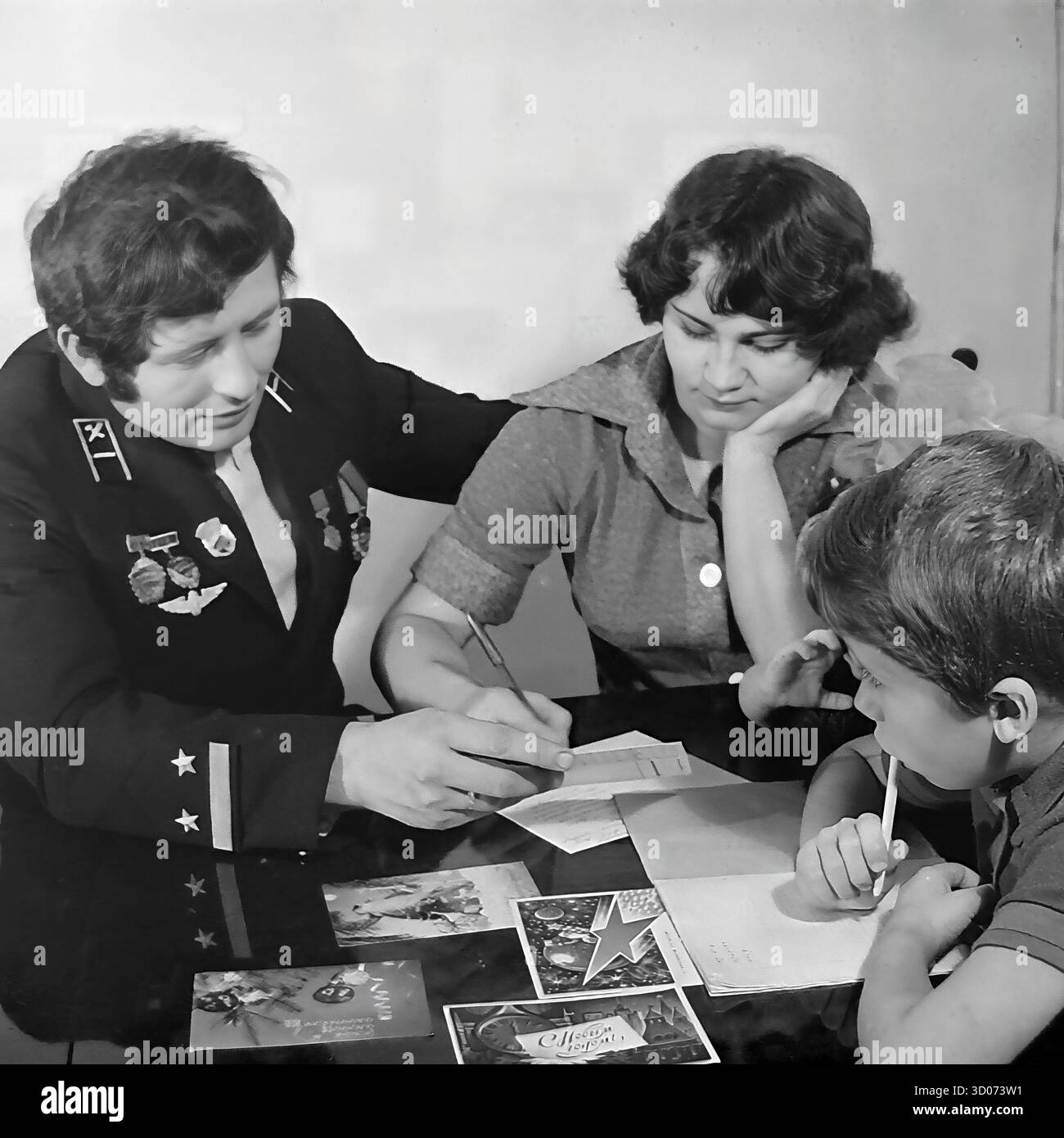 Une famille soviétique écrivant des cartes de vœux de vacances à la maison à Sloviansk, années 1970-1980s. Archive photo en noir et blanc, URSS, RSS d'Ukraine. Le père, machiniste et vétéran dans son uniforme de chemin de fer avec des médailles, est assis avec sa femme et son fils à une table. Ils signent les cartes du nouvel an ou du 23 février. Cette image réconfortante capture une scène de la vie soviétique quotidienne, des traditions familiales et de la parentalité. Un document nostalgique d'une famille heureuse et d'une vie paisible dans le Donbass avant la guerre. Banque D'Images Une famille soviétique écrivant des cartes de vœux de vacances à la maison à Sloviansk, années 1970-1980s. Archive photo en noir et blanc, URSS, RSS d'Ukraine. Le père, machiniste et vétéran dans son uniforme de chemin de fer avec des médailles, est assis avec sa femme et son fils à une table. Ils signent les cartes du nouvel an ou du 23 février. Cette image réconfortante capture une scène de la vie soviétique quotidienne, des traditions familiales et de la parentalité. Un document nostalgique d'une famille heureuse et d'une vie paisible dans le Donbass avant la guerre. Banque D'Images