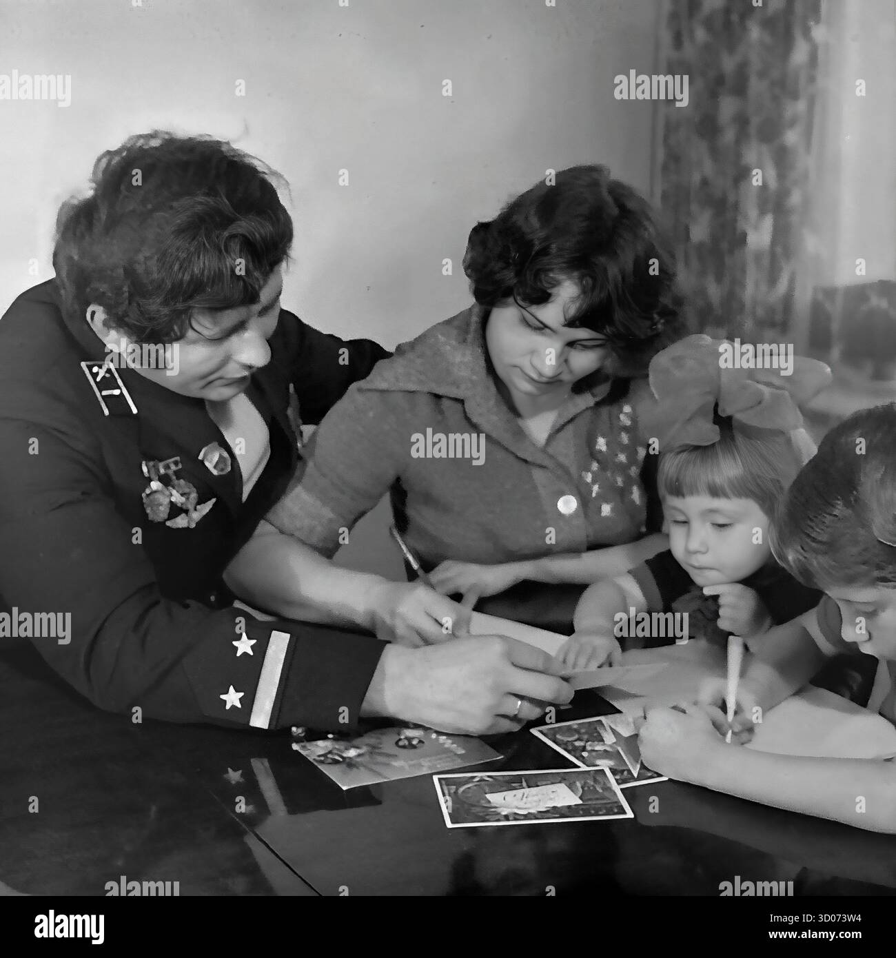 Une heureuse famille soviétique de quatre (père, mère, fils et fille) écrit des cartes de vœux de vacances à la maison à Sloviansk, années 1970-1980 Archive photo en noir et blanc, URSS, RSS d'Ukraine. Le père, machiniste et vétéran, porte son uniforme de chemin de fer officiel avec des médailles. Toute la famille est assise ensemble à la table. Les enfants écrivent aussi. Cette image réconfortante capture une scène de la vie soviétique quotidienne, des traditions familiales et de la parentalité. Un document nostalgique d'une famille heureuse et d'une vie paisible dans le Donbass avant la guerre. Banque D'Images Une heureuse famille soviétique de quatre (père, mère, fils et fille) écrit des cartes de vœux de vacances à la maison à Sloviansk, années 1970-1980 Archive photo en noir et blanc, URSS, RSS d'Ukraine. Le père, machiniste et vétéran, porte son uniforme de chemin de fer officiel avec des médailles. Toute la famille est assise ensemble à la table. Les enfants écrivent aussi. Cette image réconfortante capture une scène de la vie soviétique quotidienne, des traditions familiales et de la parentalité. Un document nostalgique d'une famille heureuse et d'une vie paisible dans le Donbass avant la guerre. Banque D'Images