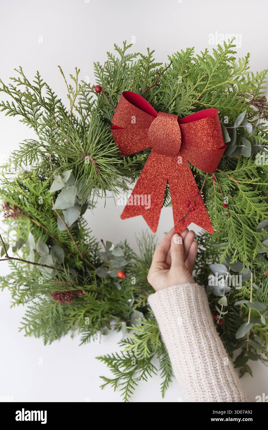 Couronne de Noël élégante pour l'intérieur, accrochez la couronne sur la porte. Fait à la main, la jeune fille tient une couronne fraîchement faite avec un joli noeud rouge. Banque D'Images