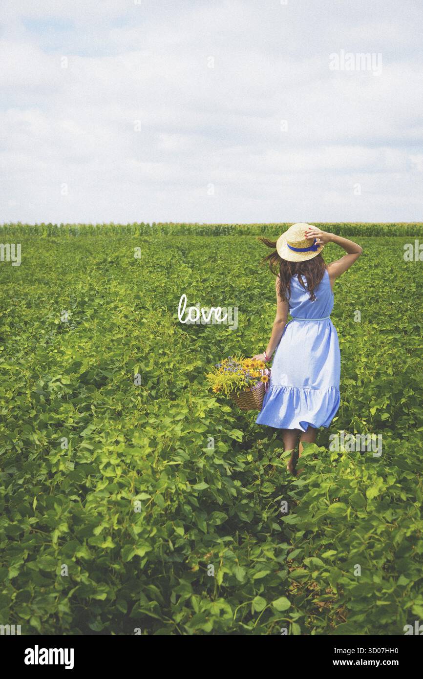 Belle fille dans un chapeau se tient dans un champ vert avec un bouquet de fleurs - inscription amour Banque D'Images