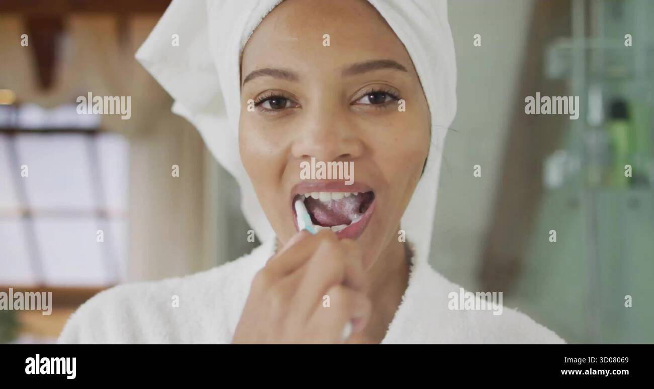 Femme d'âge moyen se brossant les dents dans la salle de bains à la maison, avec brosse à dents serviette turban et volets de fenêtre Banque D'Images