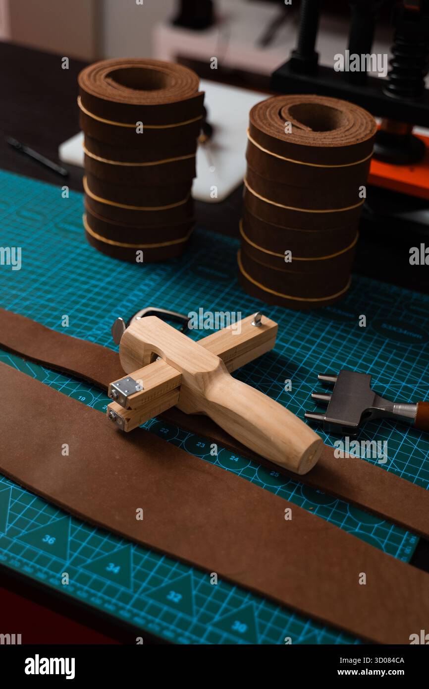 Installation de travail du cuir avec des outils, une boucle et des bandes de cuir disposées soigneusement sur un tapis, prêt pour la fabrication de ceinture. Outils de maroquinerie et fabrication de courroies p Banque D'Images