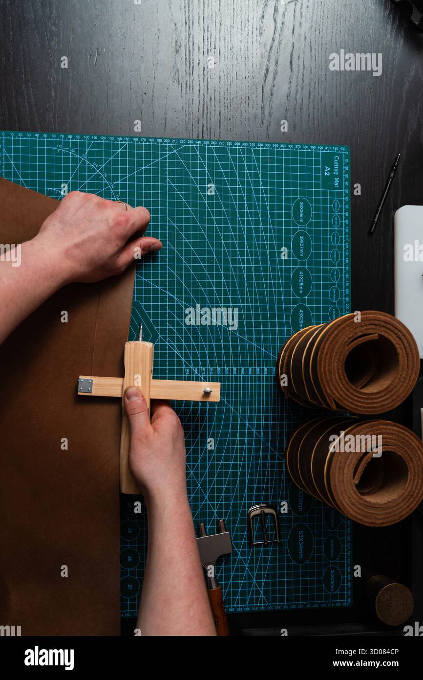 Artisan préparant le bracelet en cuir à l'aide d'un couteau en bois sur le tapis. Préparation de ceinture en cuir à la main avec coupe-sangle en bois sur le tapis de coupe. Artisan est Cu Banque D'Images