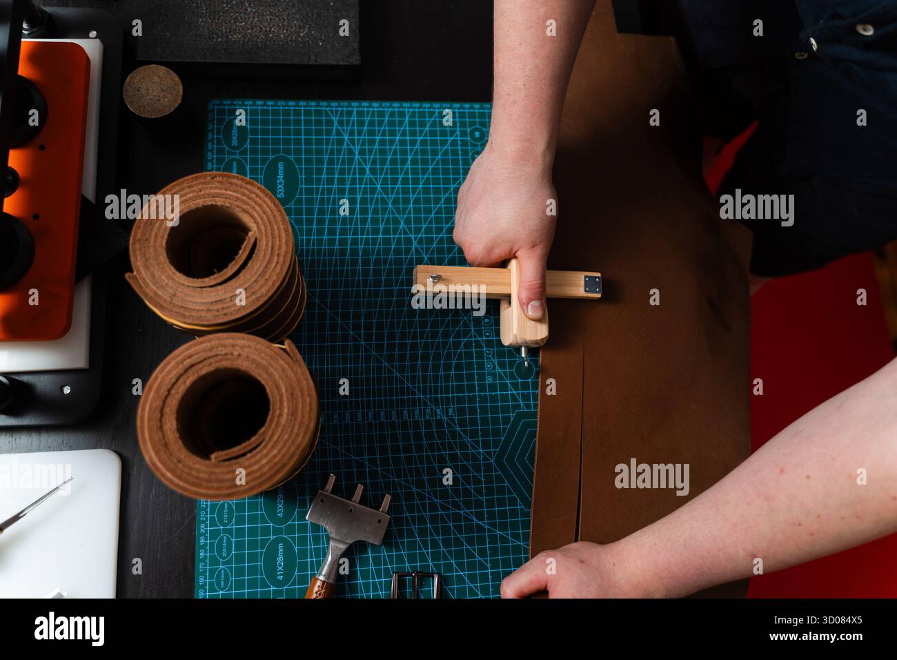 Artisan préparant le bracelet en cuir à l'aide d'un couteau en bois sur le tapis. Préparation de ceinture en cuir à la main avec coupe-sangle en bois sur le tapis de coupe. Artisan est Cu Banque D'Images