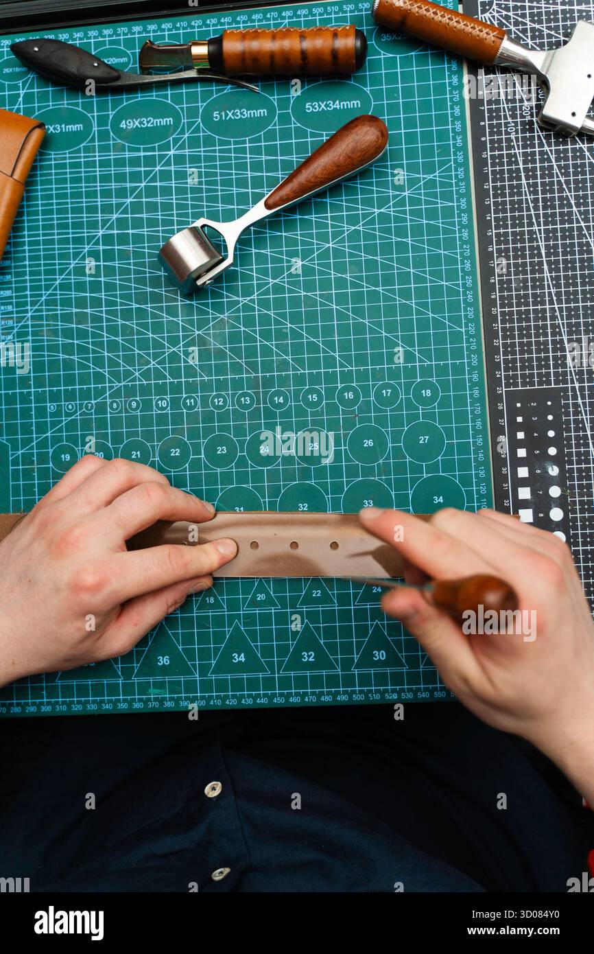 Fabrication de trous de ceinture avec outil de poinçon sur bracelet en cuir. Poinçonnage et détail des trous de ceinture en cuir. Artisan perçant des trous dans un bracelet en cuir pour un han Banque D'Images