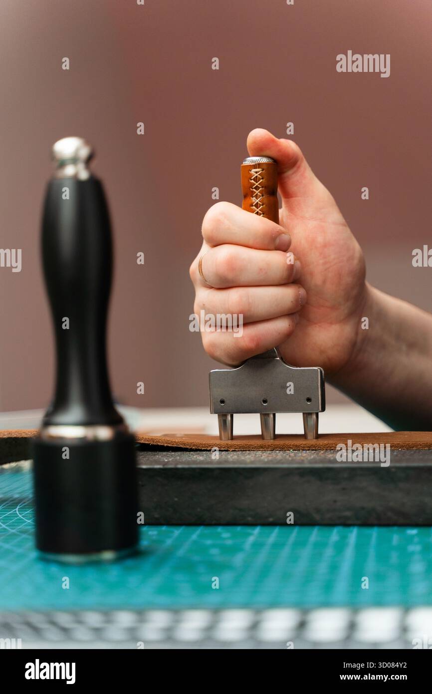 Fabrication de trous de ceinture avec outil de poinçon sur bracelet en cuir. Poinçonnage et détail des trous de ceinture en cuir. Artisan perçant des trous dans un bracelet en cuir pour un han Banque D'Images