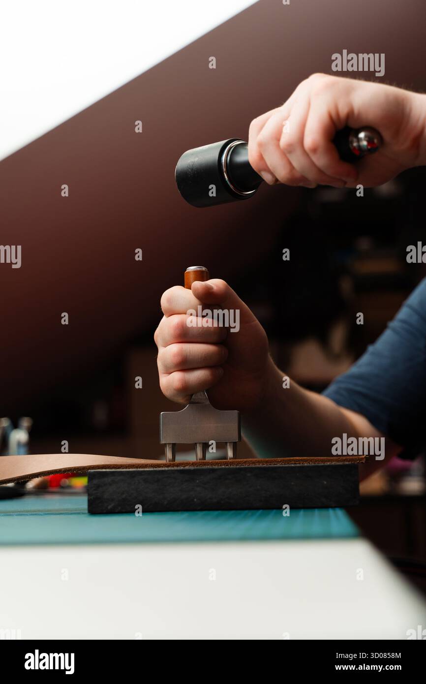 Fabrication de trous de ceinture avec outil de poinçon sur bracelet en cuir. Poinçonnage et détail des trous de ceinture en cuir. Artisan perçant des trous dans un bracelet en cuir pour un han Banque D'Images