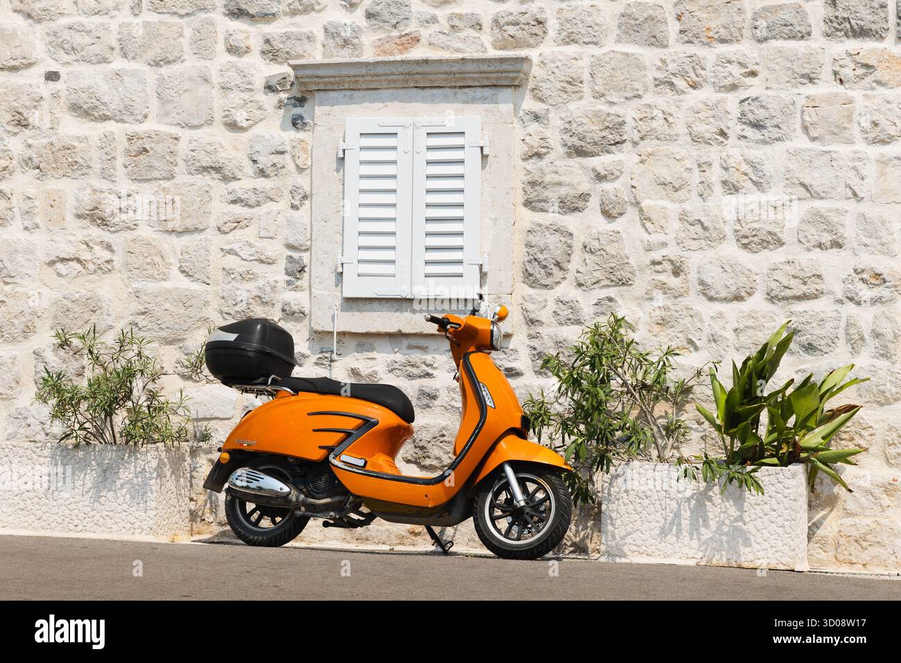 Istanbul, Turquie - 14 août 2025 : un scooter Veracruz orange vif repose à côté d'un mur de pierre texturé et d'une fenêtre blanche à volets, avec des jardinières et Banque D'Images