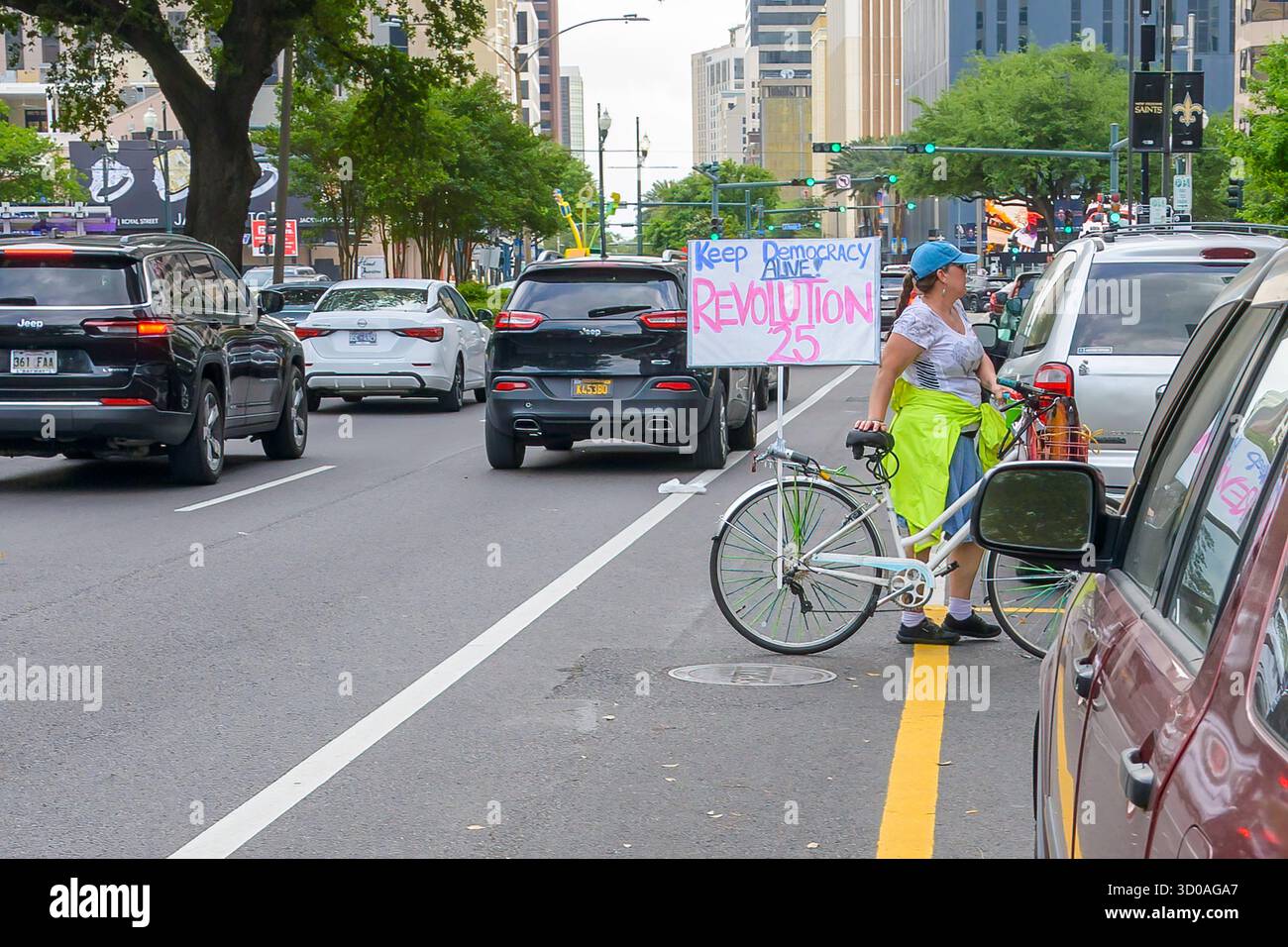 La Nouvelle-Orléans, LOUISIANE, États-Unis - 19 avril 2025 : une femme fait une pause sur la rue Poydras, devant les bureaux de l'Agence douanière de l'immigration (ICE), avec son vélo et une pancarte pour protester contre les politiques de Trump Banque D'Images