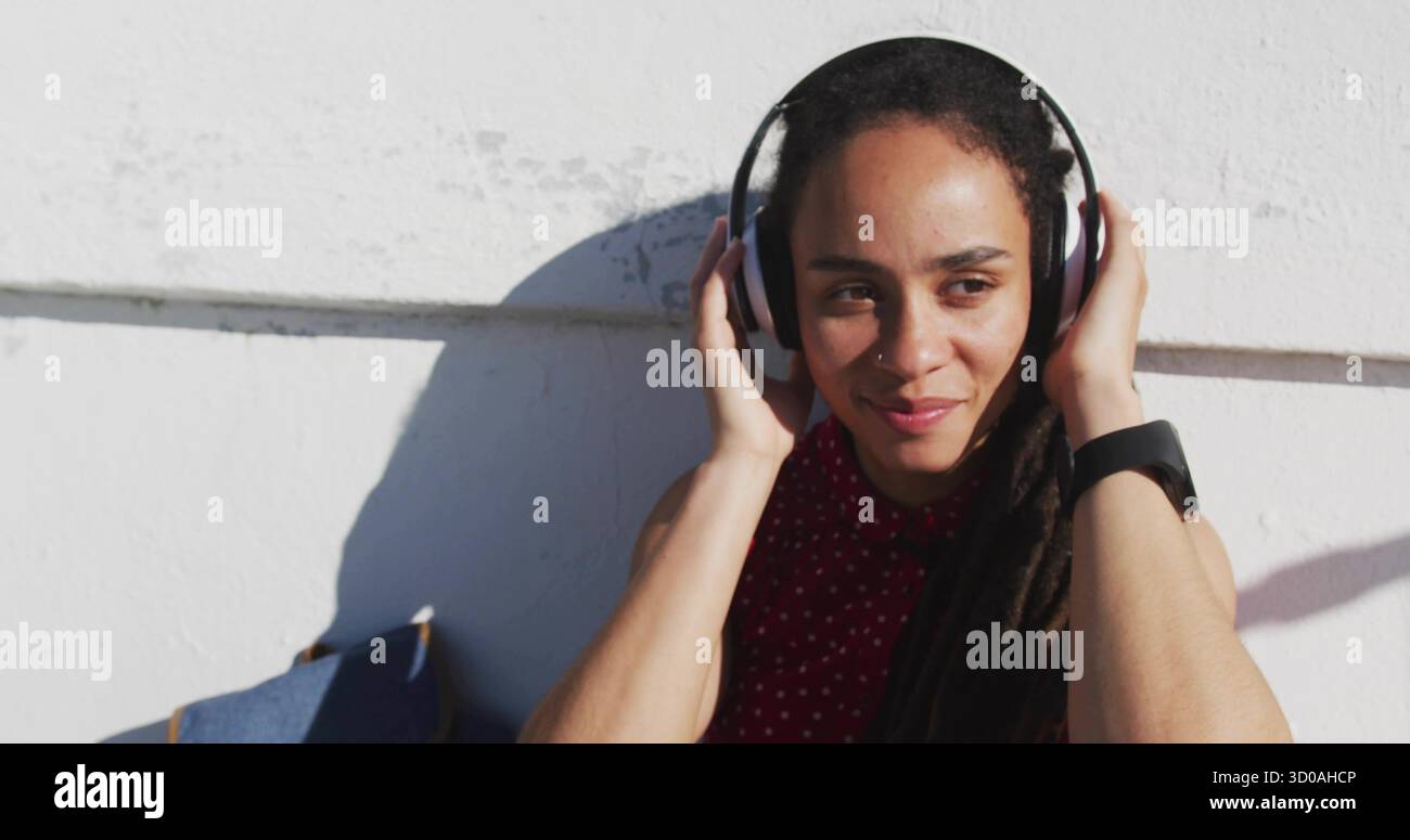 Femme en chemise rouge ajustant les écouteurs contre le mur urbain, avec smartwatch, sac bleu, espace copie Banque D'Images