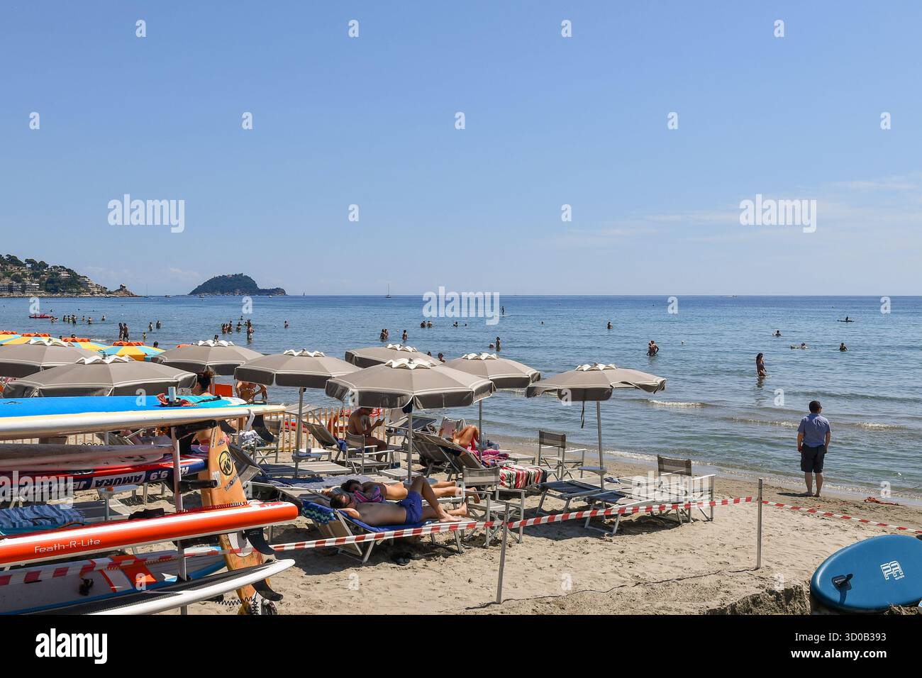 Vue sur la plage de sable avec stand-up paddleboards, clubs de plage et l'île Gallinara à l'horizon de la mer, en été, Alassio (Savone), Ligurie, Italie Banque D'Images