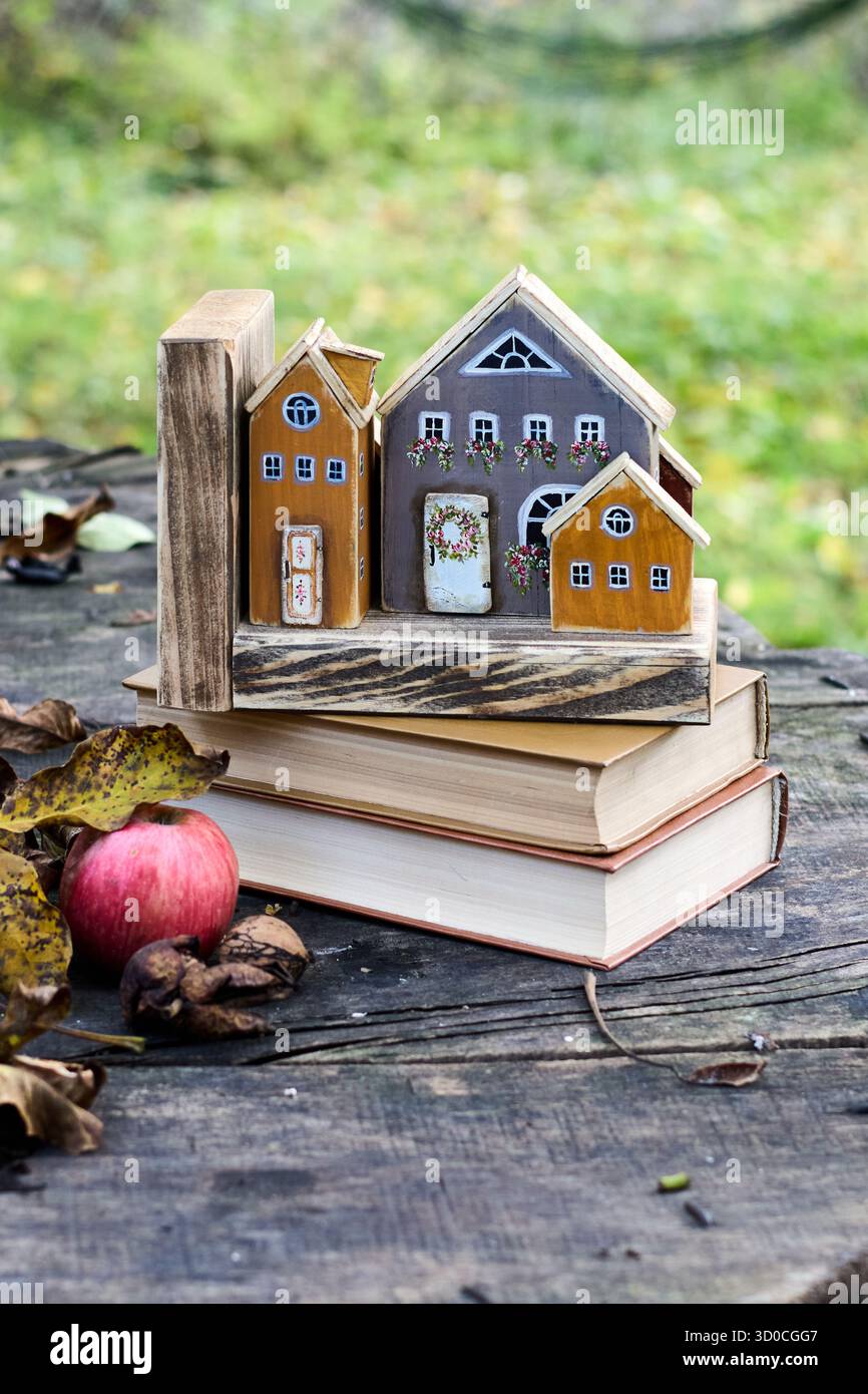 Nature morte d'automne confortable : maisons de jouet en bois, livres, pomme et noix sur une surface en bois, créant une scène chaleureuse et accueillante. Banque D'Images
