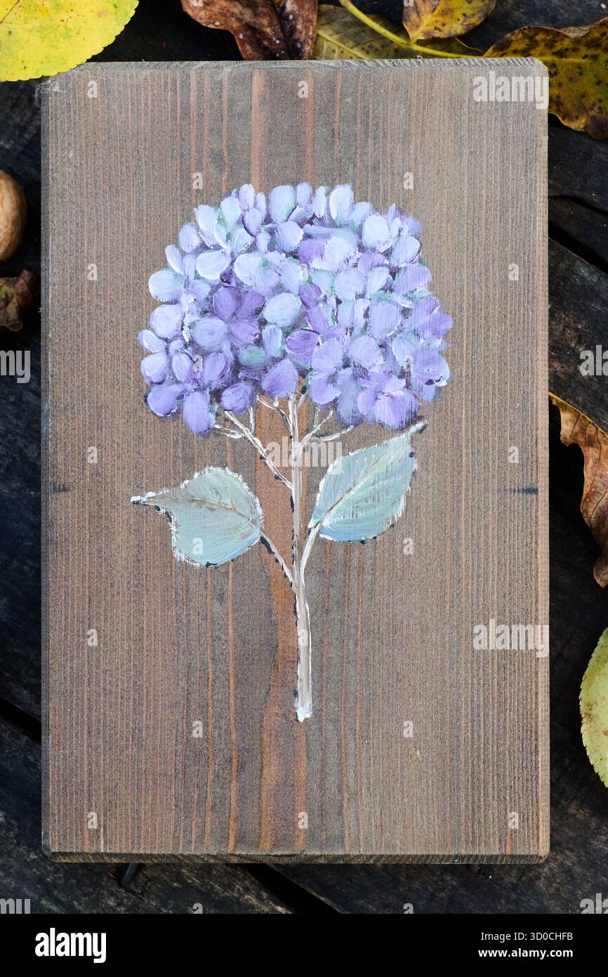 L'hortensia pourpre fleurit sur une planche de bois, mettant en valeur un mélange d'expression artistique et de beauté naturelle dans un cadre rustique avec des feuilles à proximité. Banque D'Images