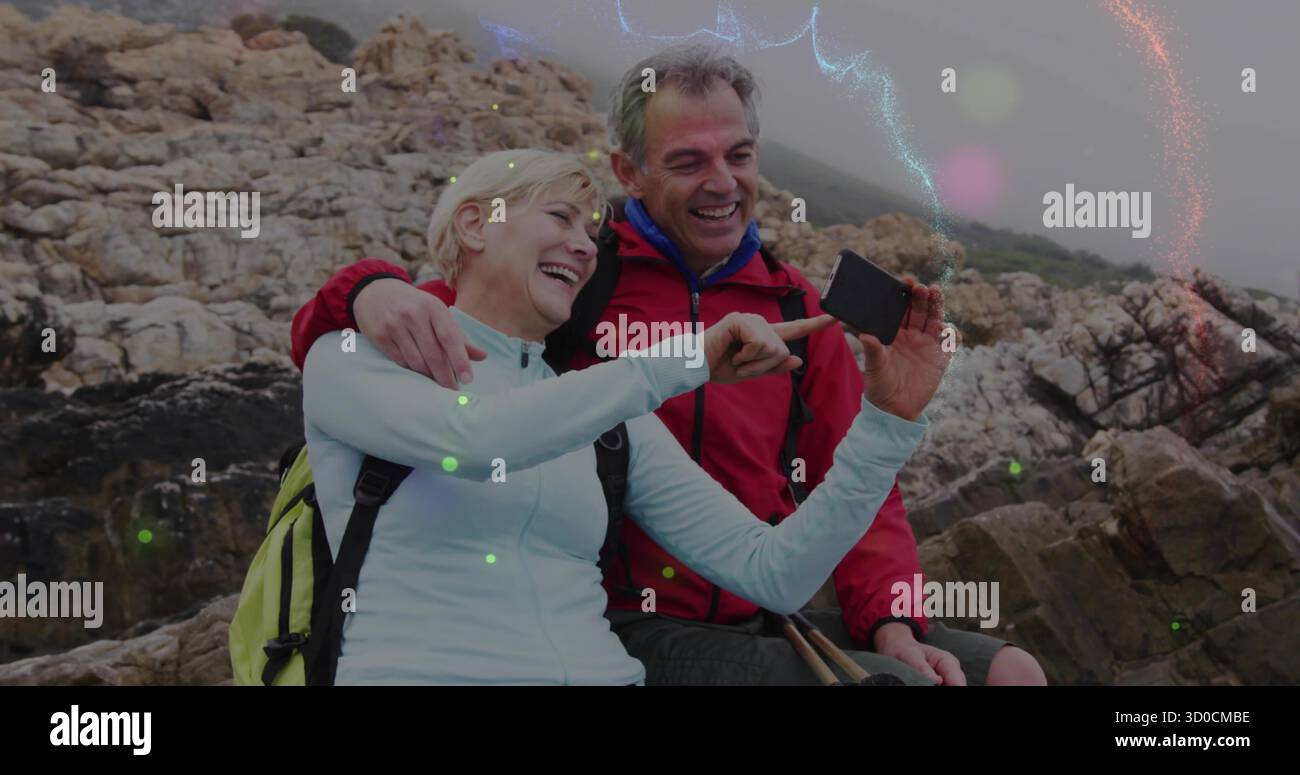 Posant couple portant des équipements d'extérieur sur l'affleurement côtier rocheux, tenant smartphone et bâtons de randonnée Banque D'Images
