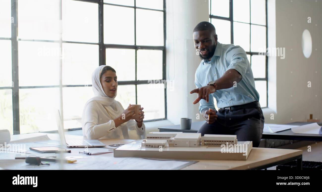 Architectes collaborant discutant du modèle réduit à la table du studio de design, avec des plans et un ordinateur portable Banque D'Images