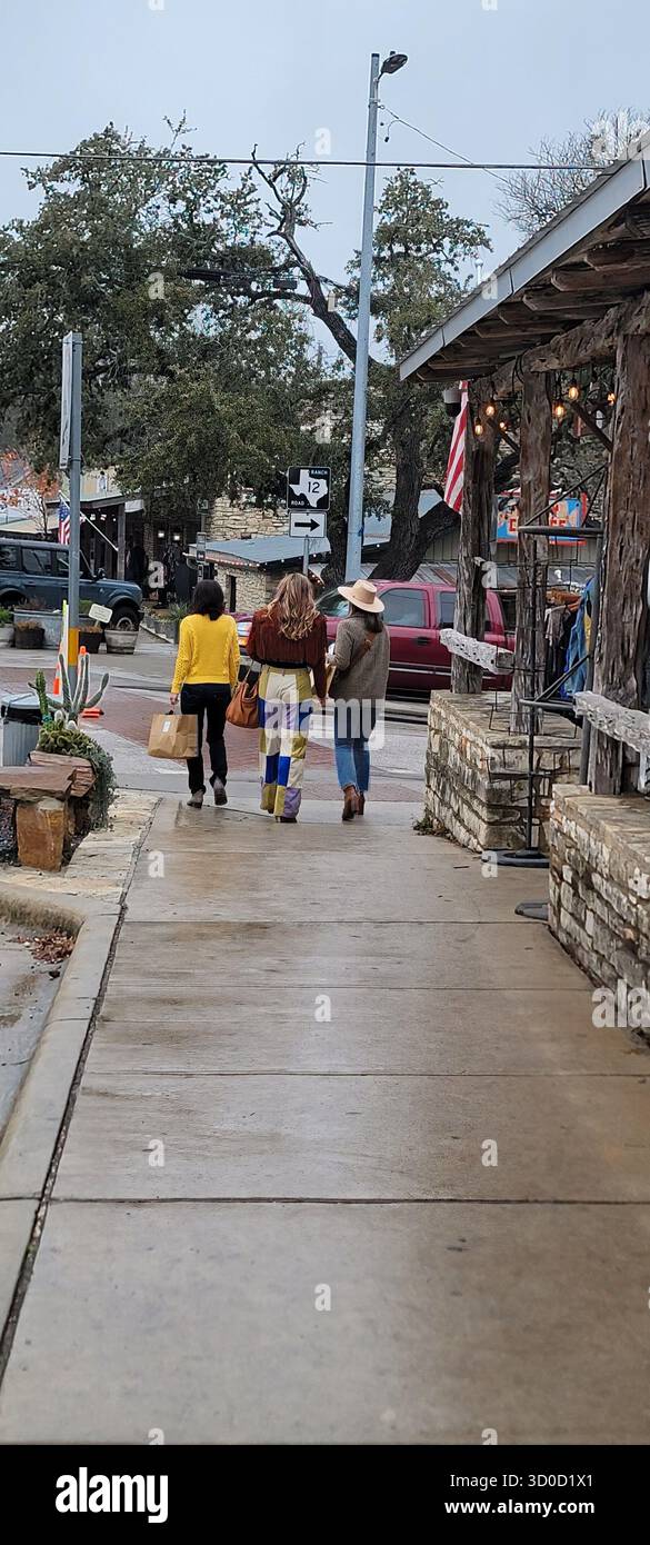 Trois amis dans le style Boho-Cowgirl marchant avec des sacs à provisions à Wimberley, Texas Banque D'Images
