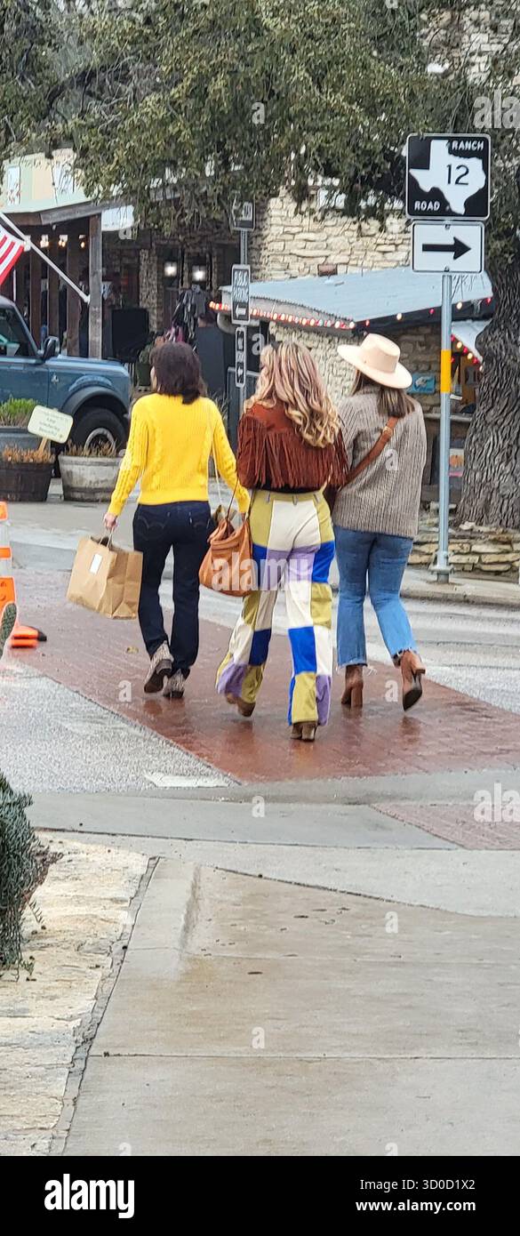 Trois amis dans le style Boho-Cowgirl marchant avec des sacs à provisions à Wimberley, Texas Banque D'Images