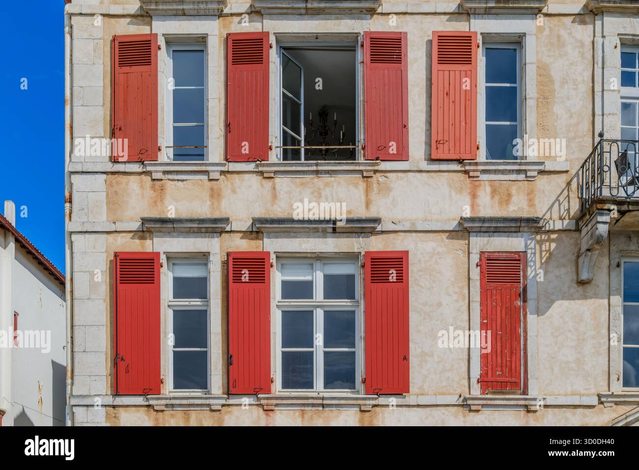 Architecture française traditionnelle, façade de bâtiment en pierre beige avec volets en bois rouge vif, cadres de fenêtre blancs, extérieur vieilli, style européen Banque D'Images
