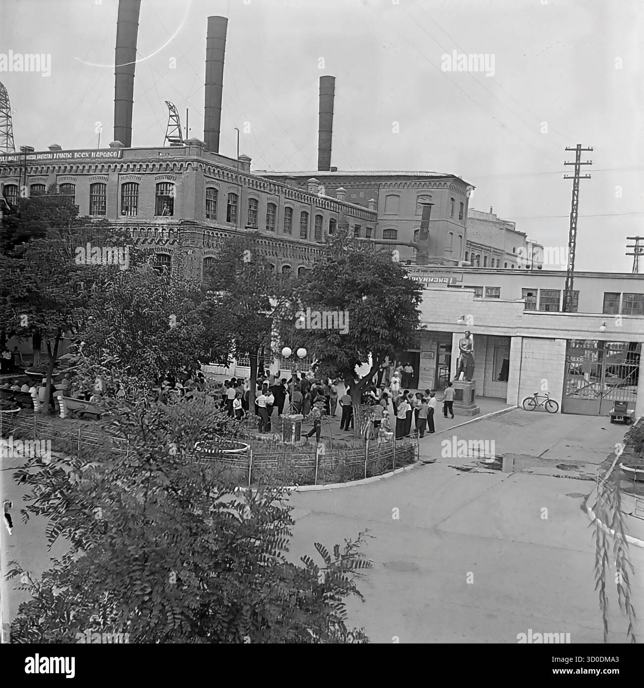 Une vue aérienne à angle élevé de l'entrée principale (prokhodnaya) de l'armature-Insulator Plant (AIZ) à Sloviansk, dans les années 1970 Cette photo d'archives en noir et blanc de l'URSS, la RSS d'Ukraine, montre une grande foule de travailleurs rassemblés sur la place de l'usine pour une célébration (des ballons sont visibles). L'arrière-plan est dominé par les bâtiments historiques massifs d'ateliers en briques (tsekh) avec de hauts cheminées. Cette image capture le paysage industriel soviétique classique et l'usine comme centre de la vie sociale. Un document précieux de la vie industrielle pacifique dans le Donbass avant la guerre Banque D'Images