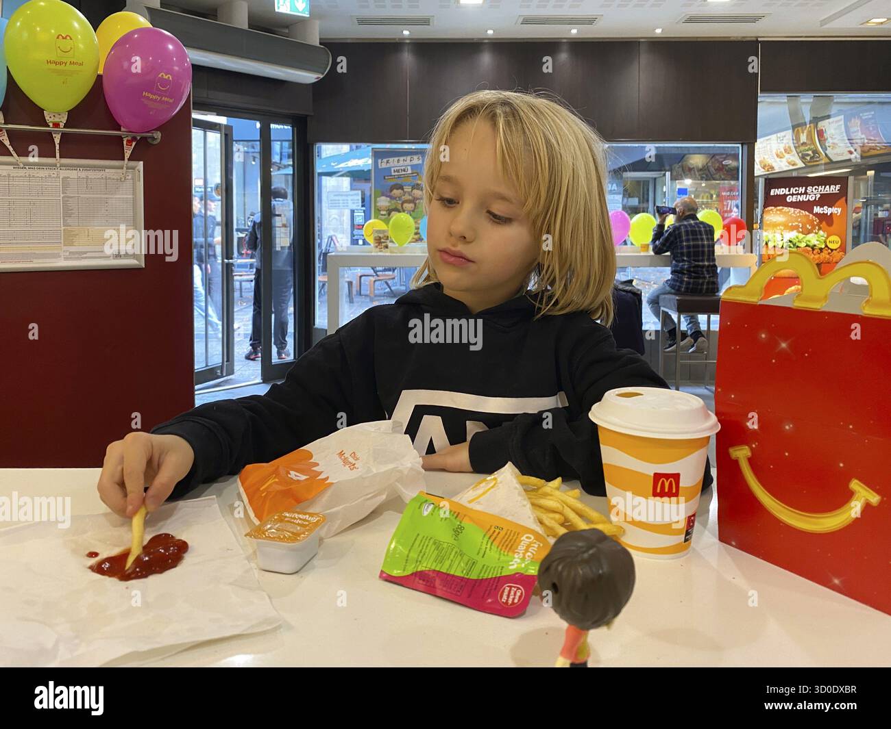 Vue intérieure, enfant, garçon, 7 ans, blonde, manger Happy Meal, menu enfant, au restaurant McDonald's, boisson, frites, ketchup, ballons, logo Banque D'Images Vue intérieure, enfant, garçon, 7 ans, blonde, manger Happy Meal, menu enfant, au restaurant McDonald's, boisson, frites, ketchup, ballons, logo Banque D'Images