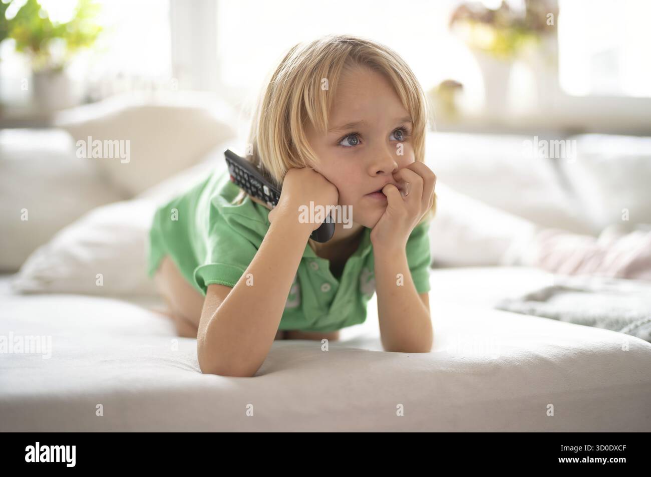 Enfant, garçon, 7 ans, blond, couché sur un canapé avec télécommande en main, regardant la télévision, regardant la télévision devant la télévision, excité, fasciné Banque D'Images Enfant, garçon, 7 ans, blond, couché sur un canapé avec télécommande en main, regardant la télévision, regardant la télévision devant la télévision, excité, fasciné Banque D'Images