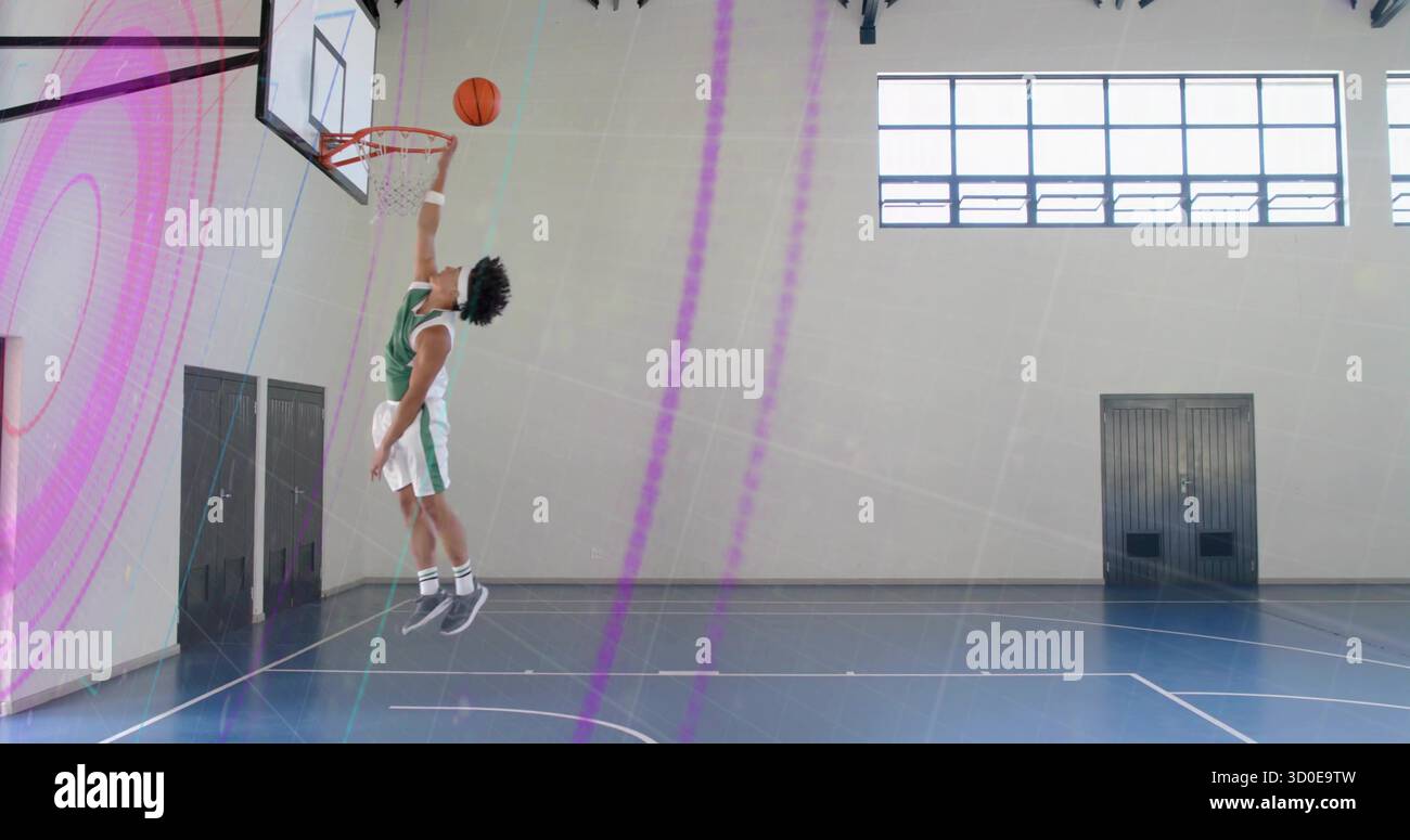 Joueur sautant portant un maillot vert exécutant un dunk sur le terrain de gym, avec panier de basket-ball, espace copie Banque D'Images