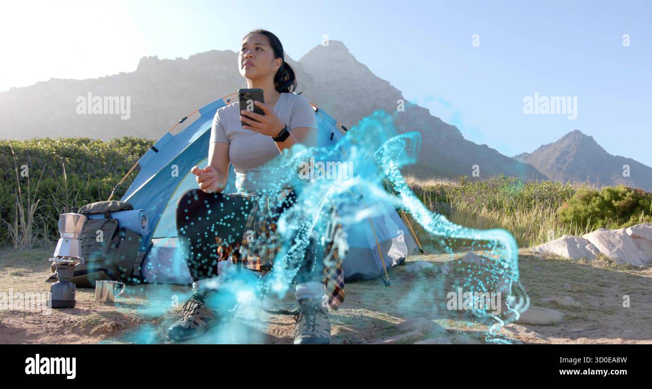 Campeur gestuel tenant un smartphone et projetant un hologramme d'eau au camping avec tente et équipement Banque D'Images