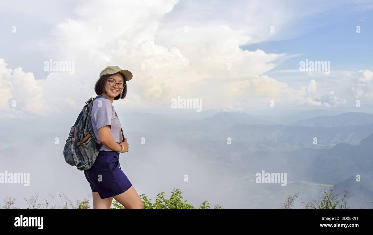 Adolescent fille randonneur porter une casquette et des lunettes avec sac à dos est debout et souriant joyeusement sur la haute montagne au point pittoresque de Phu Chi Fa Forest Park en CH Banque D'Images