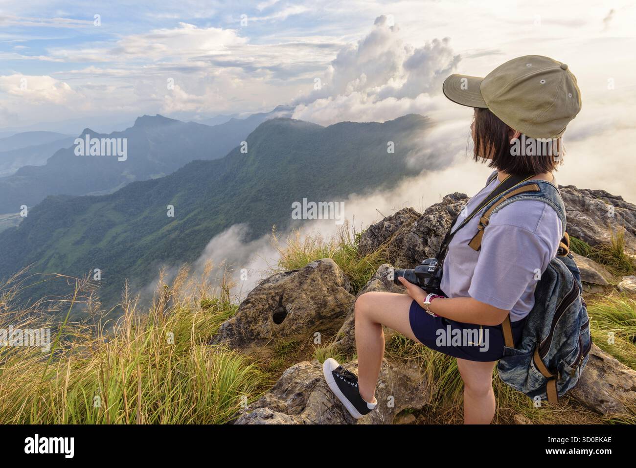 Randonneur asiatique jeune femme heureuse avec sac à dos appareil photo et casquettes regardant belle nature de paysage de montagne et de ciel au coucher du soleil sur le point de vue Phu Chi Fa F. Banque D'Images
