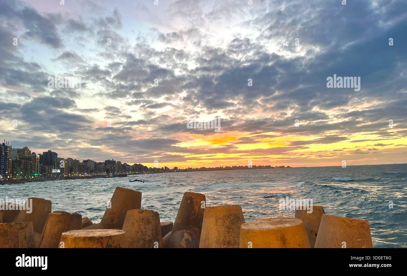 Magnifique coucher de soleil sur la mer Méditerranée à Alexandrie, en Égypte, avec une lumière dorée qui se reflète sur l'eau et l'horizon de la ville. - Image de stock capturée avec un smartphone